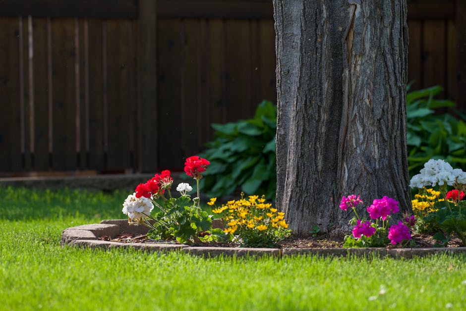 A vibrant backyard garden showcasing colorful flowers around a tree trunk.